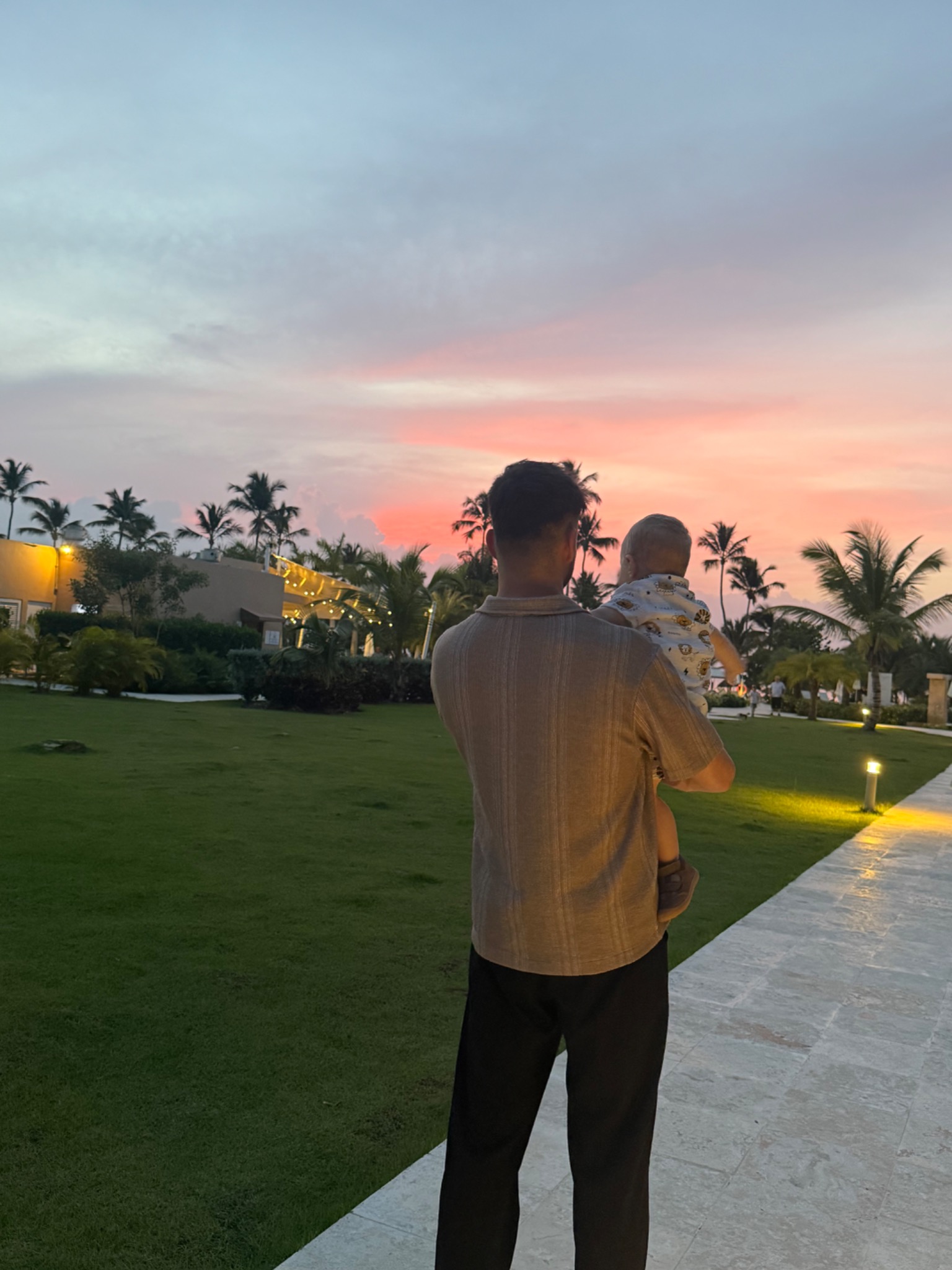 Fabian trägt sein Kind auf dem Arm und blickt mit ihm in den Sonnenuntergang